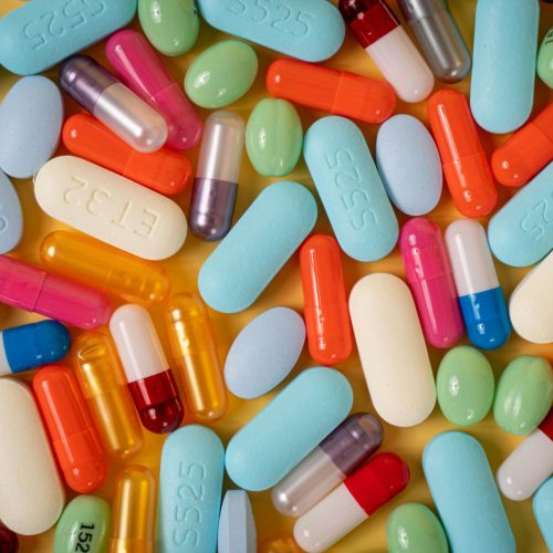 A vibrant array of various pills and capsules on a yellow background.
