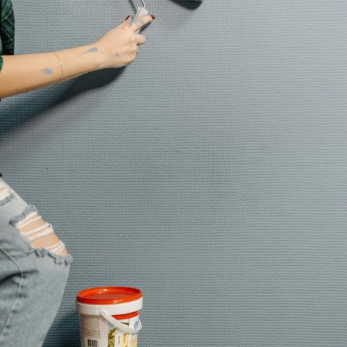 An adult painting a textured wall with a paint roller during home renovation.